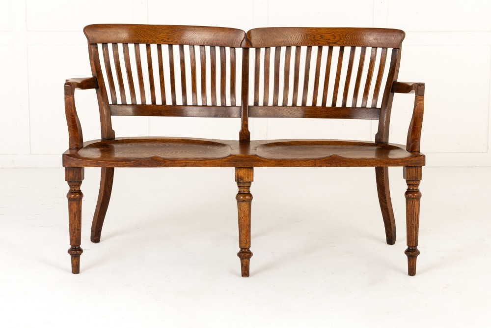 A 19th-century English oak double chair-back settee featuring twin slatted backrests, shaped seats, curved armrests, turned front legs, and splayed rear legs. View II