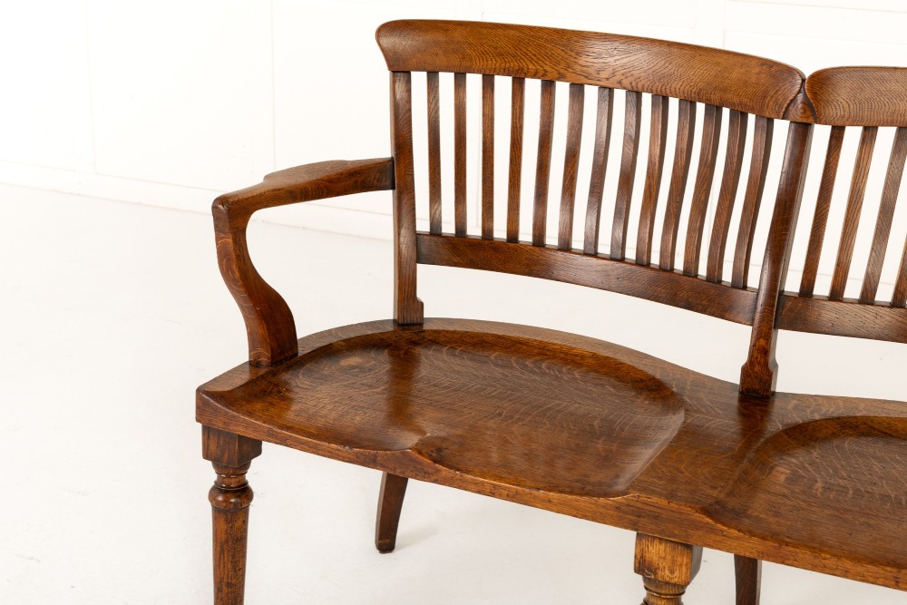 A 19th-century English oak double chair-back settee featuring twin slatted backrests, shaped seats, curved armrests, turned front legs, and splayed rear legs. View IV
