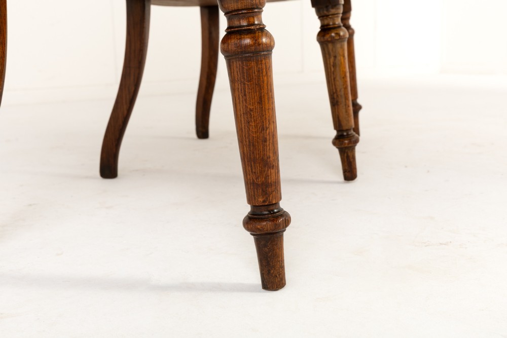 A 19th-century English oak double chair-back settee featuring twin slatted backrests, shaped seats, curved armrests, turned front legs, and splayed rear legs. View VII