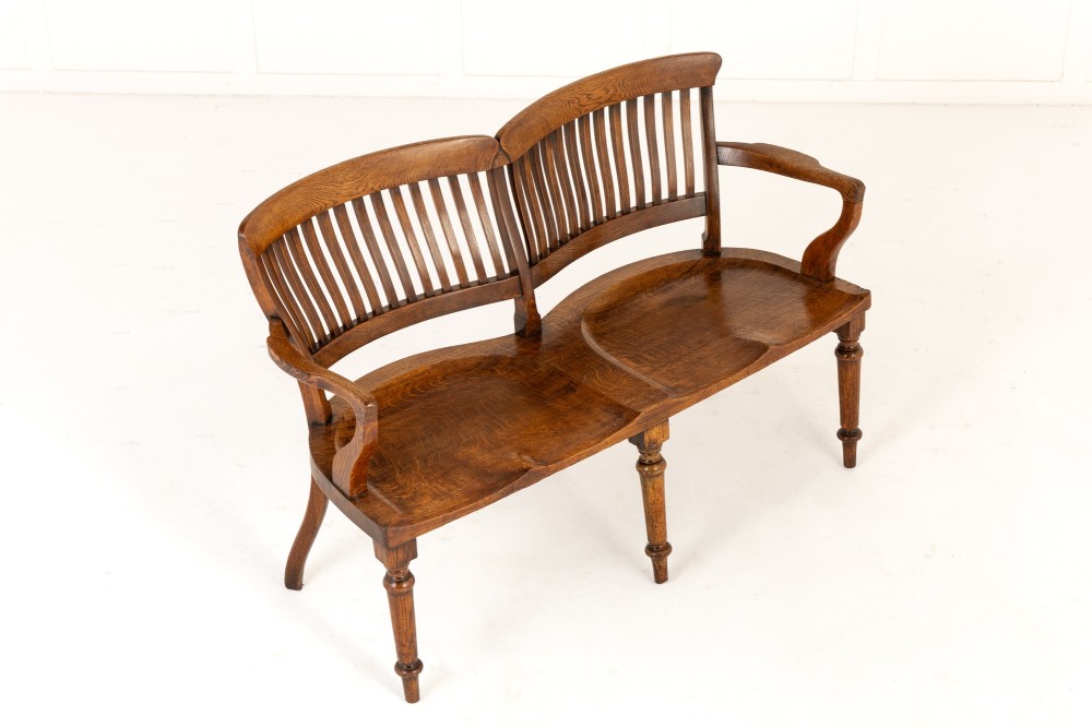 A 19th-century English oak double chair-back settee featuring twin slatted backrests, shaped seats, curved armrests, turned front legs, and splayed rear legs. View VIII