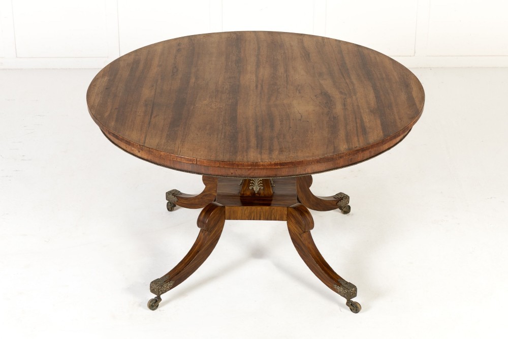A nineteenth-century Regency circular centre table made of rosewood with a quadripod pedestal base on brass castors.