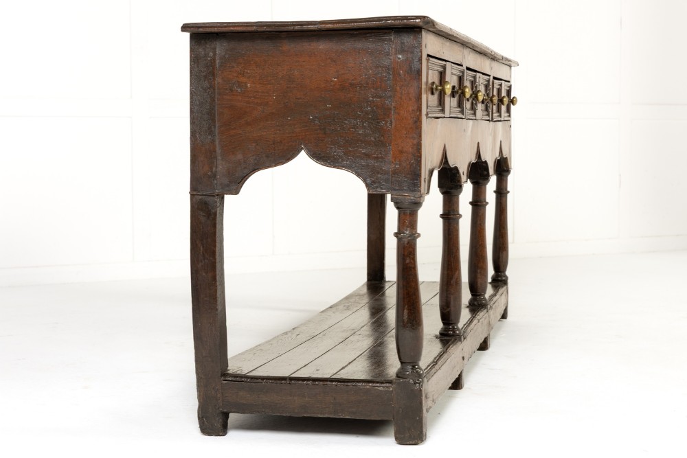 An 18th-century dark oak dresser base featuring geometric panelled drawer fronts, a shaped lower apron, turned front legs, and a bottom potboard shelf. View II