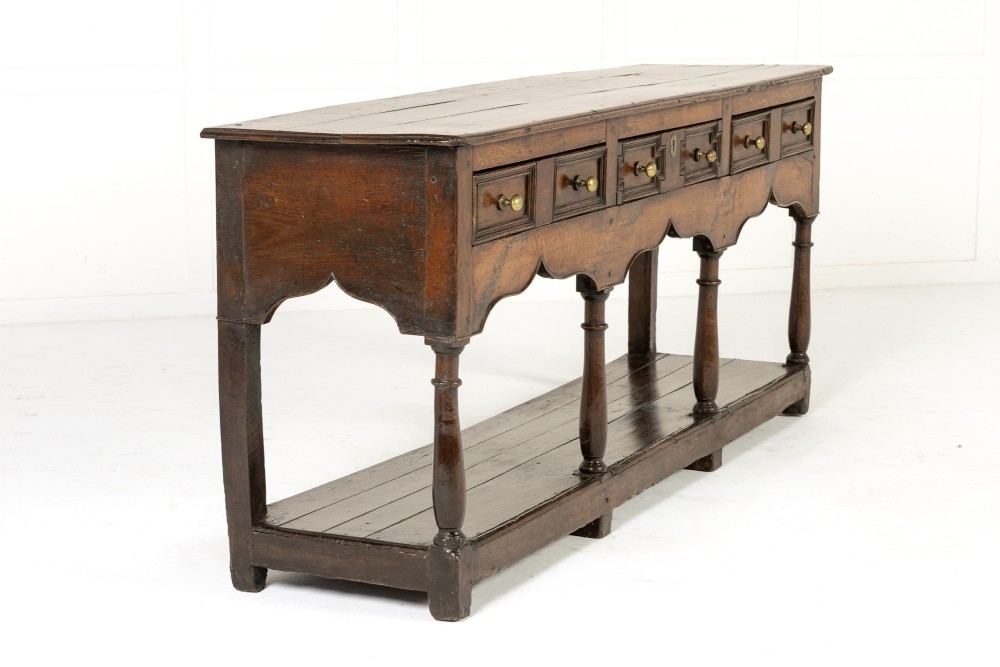 An 18th-century dark oak dresser base featuring geometric panelled drawer fronts, a shaped lower apron, turned front legs, and a bottom potboard shelf. View III