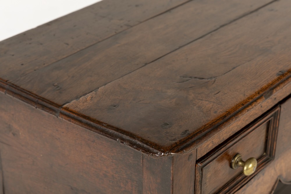 An 18th-century dark oak dresser base featuring geometric panelled drawer fronts, a shaped lower apron, turned front legs, and a bottom potboard shelf. View IV