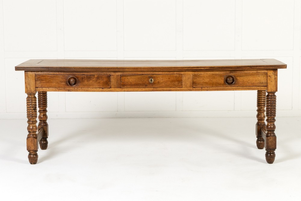 A 19th-century French walnut drapers table with three drawers, wooden knobs, a central keyhole, and turned legs with lower stretchers.