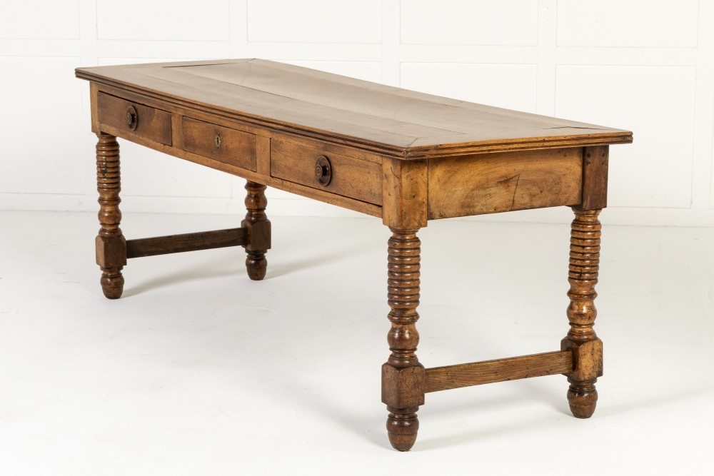 A 19th-century French walnut drapers table with three drawers, wooden knobs, a central keyhole, and turned legs with lower stretchers. View IX