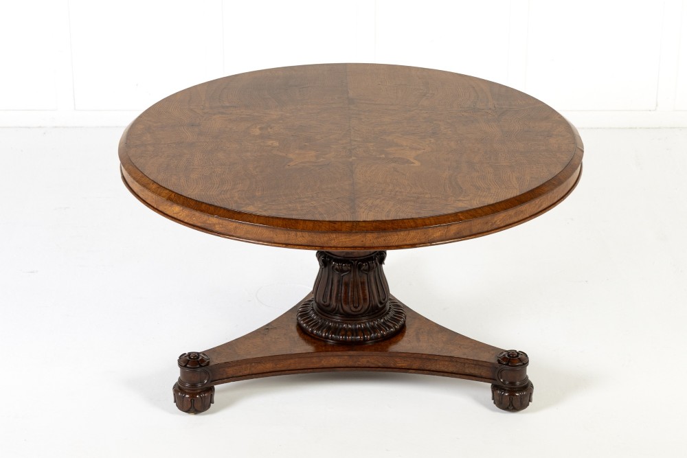 An early nineteenth-century circular centre table featuring a figured burr oak top mounted on a carved central column and a tri-form base with carved feet.