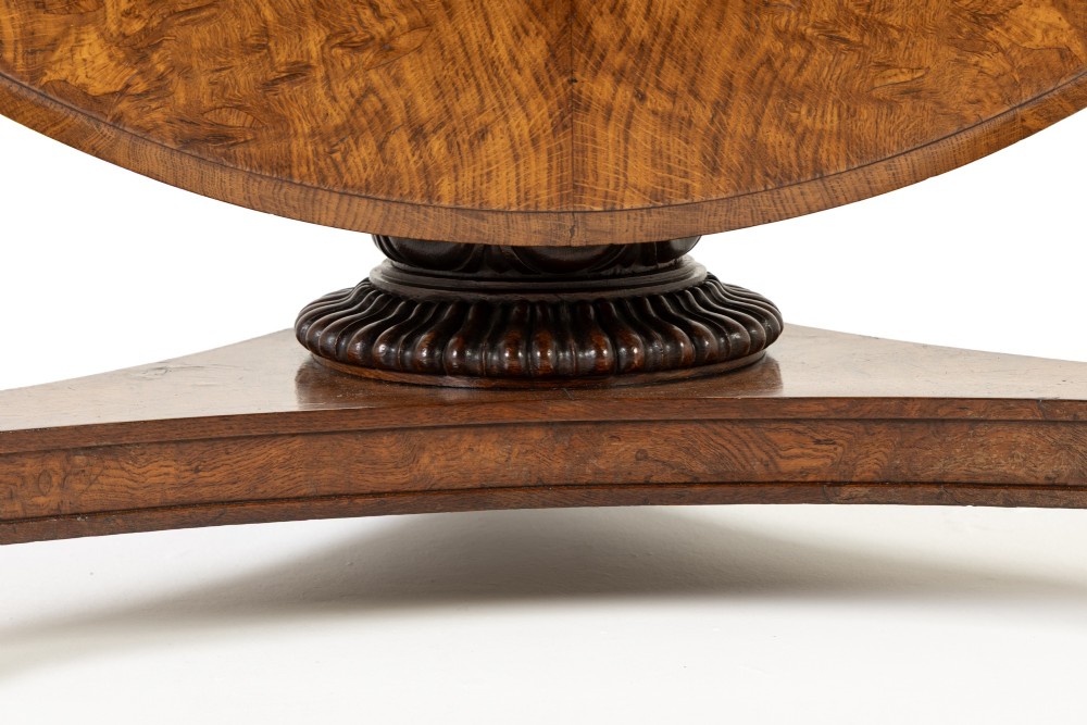 An early nineteenth-century circular centre table featuring a figured burr oak top mounted on a carved central column and a tri-form base with carved feet. View II