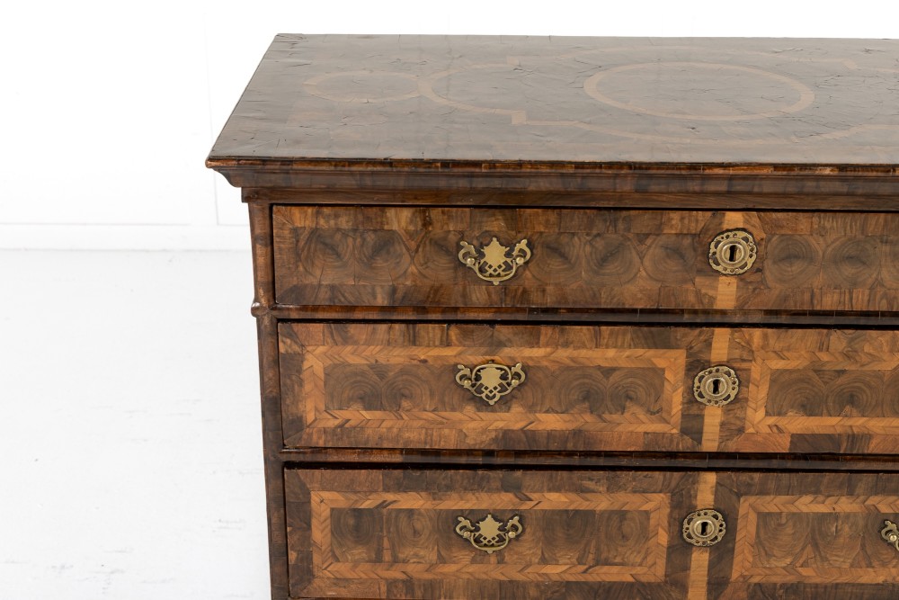 A late 17th-century Dutch walnut chest of drawers featuring geometric oyster veneering, brass drop handles, keyhole escutcheons, and large turned bun feet. View III