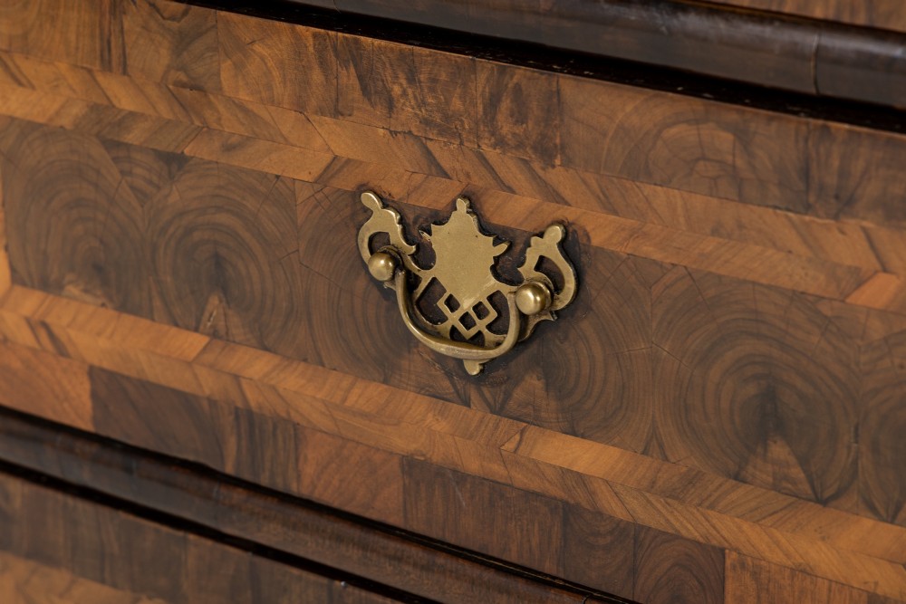 A late 17th-century Dutch walnut chest of drawers featuring geometric oyster veneering, brass drop handles, keyhole escutcheons, and large turned bun feet. View VI