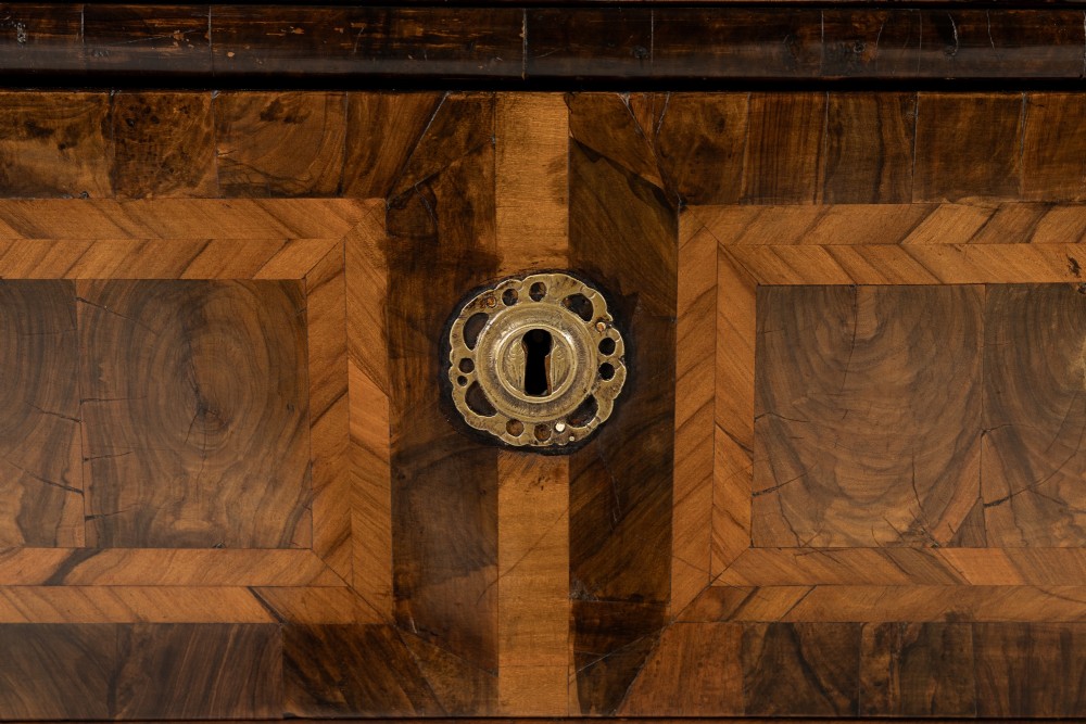 A late 17th-century Dutch walnut chest of drawers featuring geometric oyster veneering, brass drop handles, keyhole escutcheons, and large turned bun feet. View VII