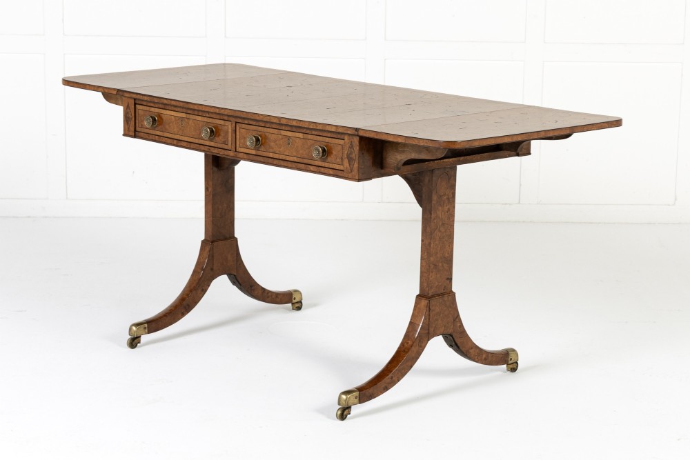 A 19th-century warm brown elm sofa table with two drop leaves, two frieze drawers, twin pedestal supports, and brass castors.