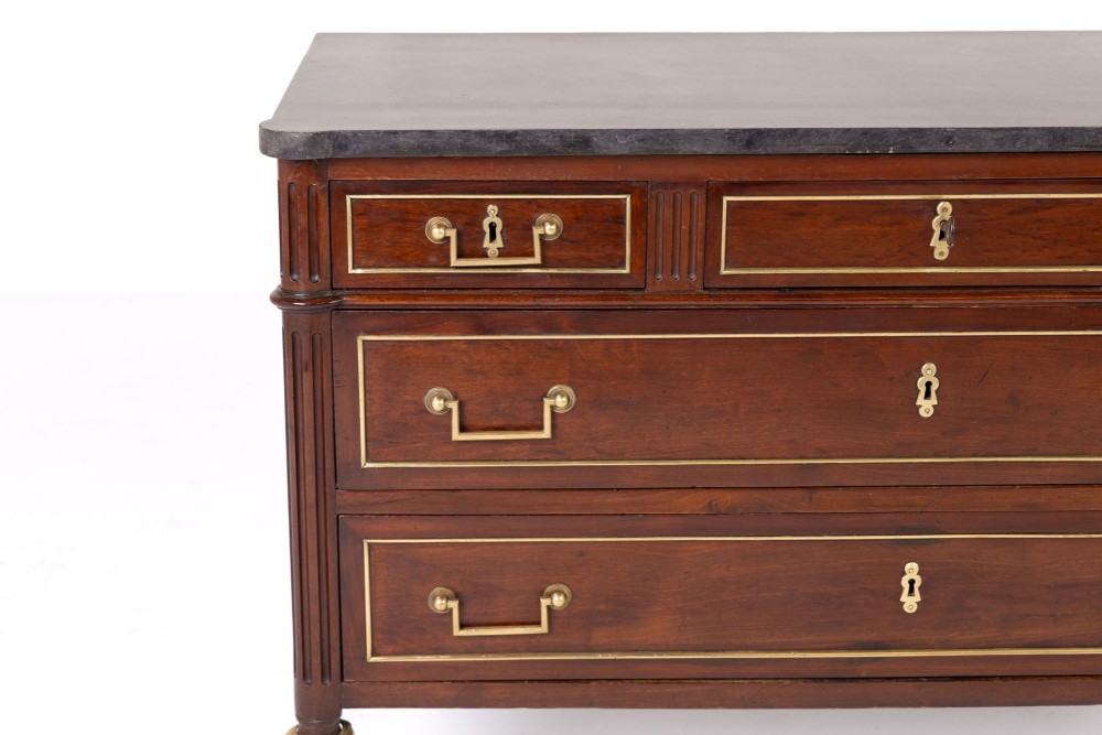 An 18th-century French mahogany commode featuring three upper short drawers, two long lower drawers with brass moulding, turned fluted legs, and a dark marble top. View II