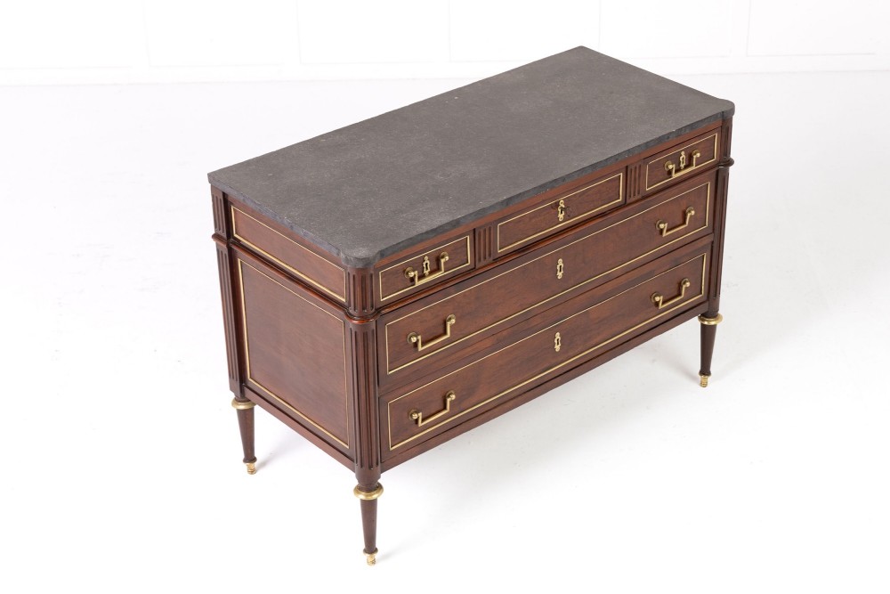 An 18th-century French mahogany commode featuring three upper short drawers, two long lower drawers with brass moulding, turned fluted legs, and a dark marble top. View III