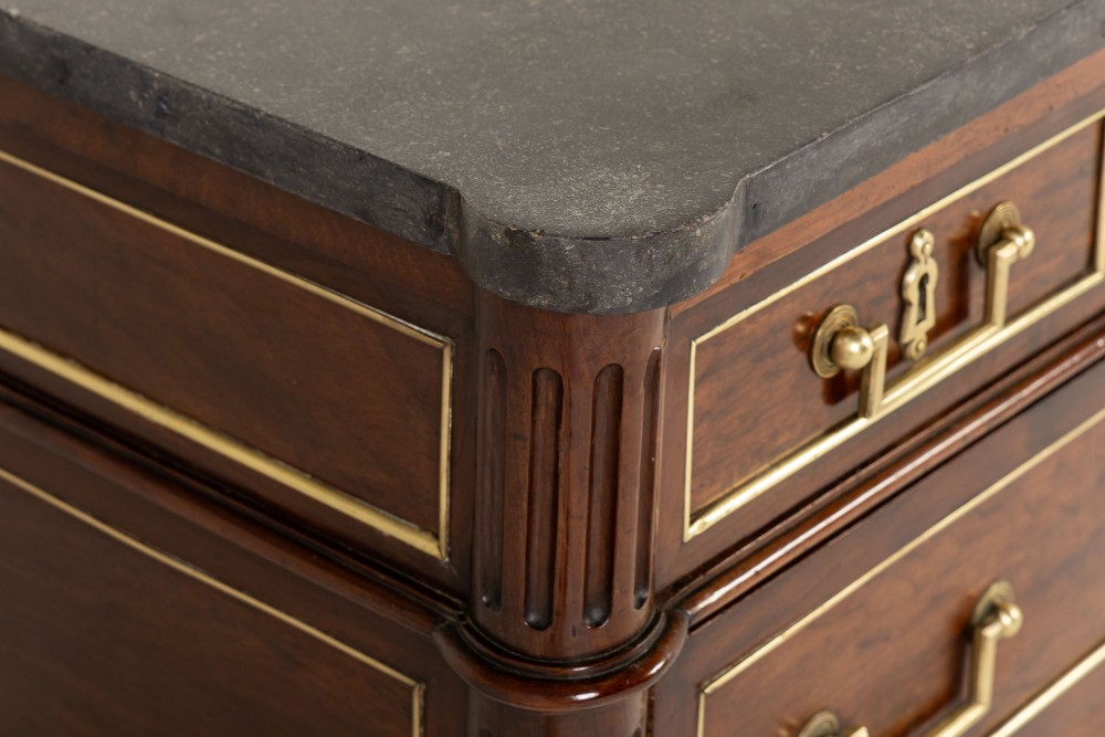 An 18th-century French mahogany commode featuring three upper short drawers, two long lower drawers with brass moulding, turned fluted legs, and a dark marble top. View VIII