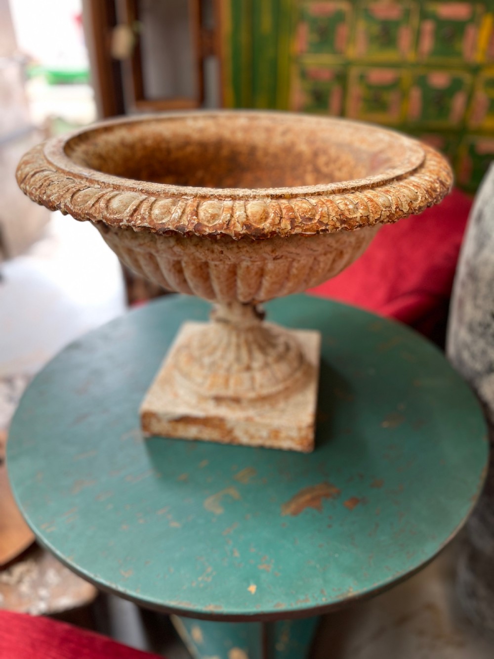 A 19th-century cast iron Ferndale garden urn featuring a gadrooned bowl and fluted rim with a distressed cream painted finish on a square pedestal base.