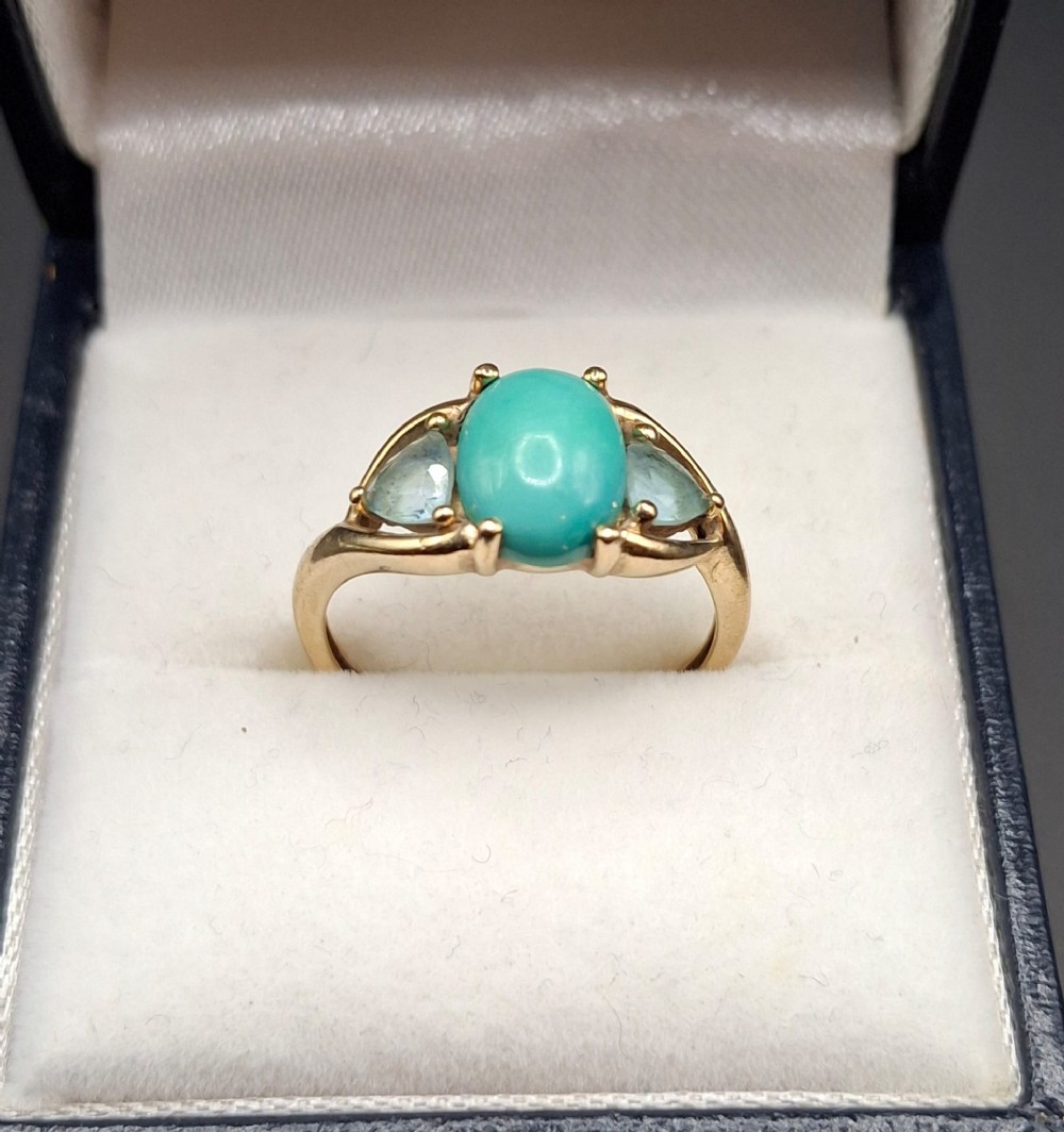 A 9ct yellow gold ring featuring an oval cabochon turquoise flanked by two triangular blue topaz gemstones in claw settings.