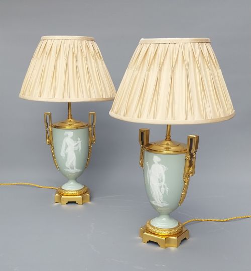 fig 1. A pair of 19th-century French celadon green porcelain urn table lamps featuring white pate-sur-pate classical relief figures, gilt bronze handles and bases, and cream pleated lampshades.