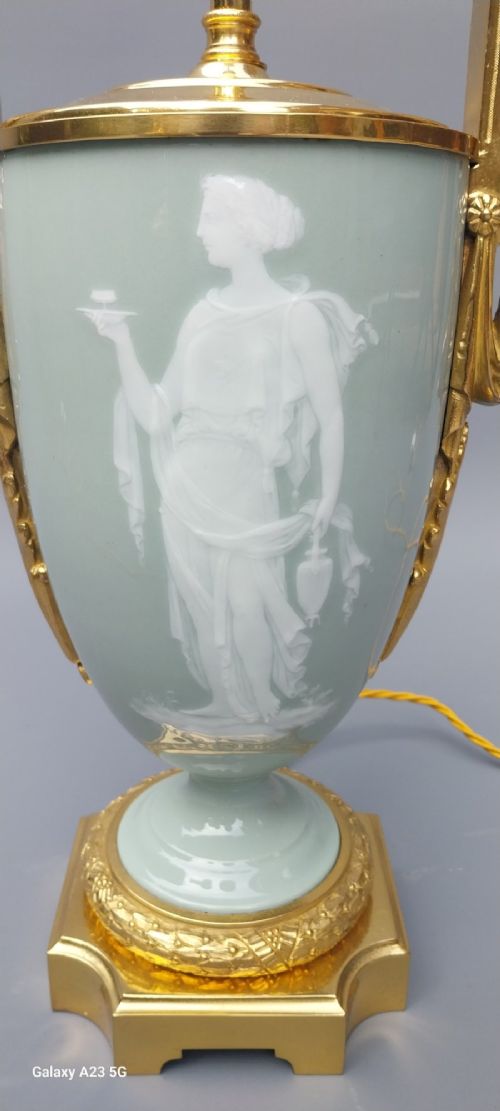 A pair of 19th-century French celadon green porcelain urn table lamps featuring white pate-sur-pate classical relief figures, gilt bronze handles and bases, and cream pleated lampshades. View IX