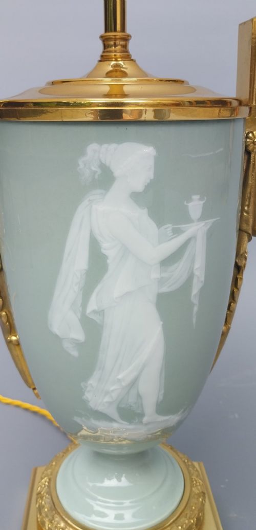 A pair of 19th-century French celadon green porcelain urn table lamps featuring white pate-sur-pate classical relief figures, gilt bronze handles and bases, and cream pleated lampshades. View XII