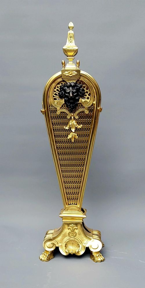 fig 1. A French gilt bronze fan-shaped fire screen featuring folding filigree mesh panels, an ornate central standard with a dark mask, and a cast shell pedestal base.