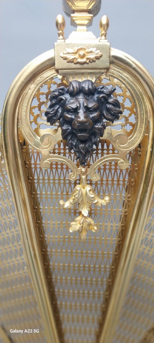 A French gilt bronze fan-shaped fire screen featuring folding filigree mesh panels, an ornate central standard with a dark mask, and a cast shell pedestal base. View VI