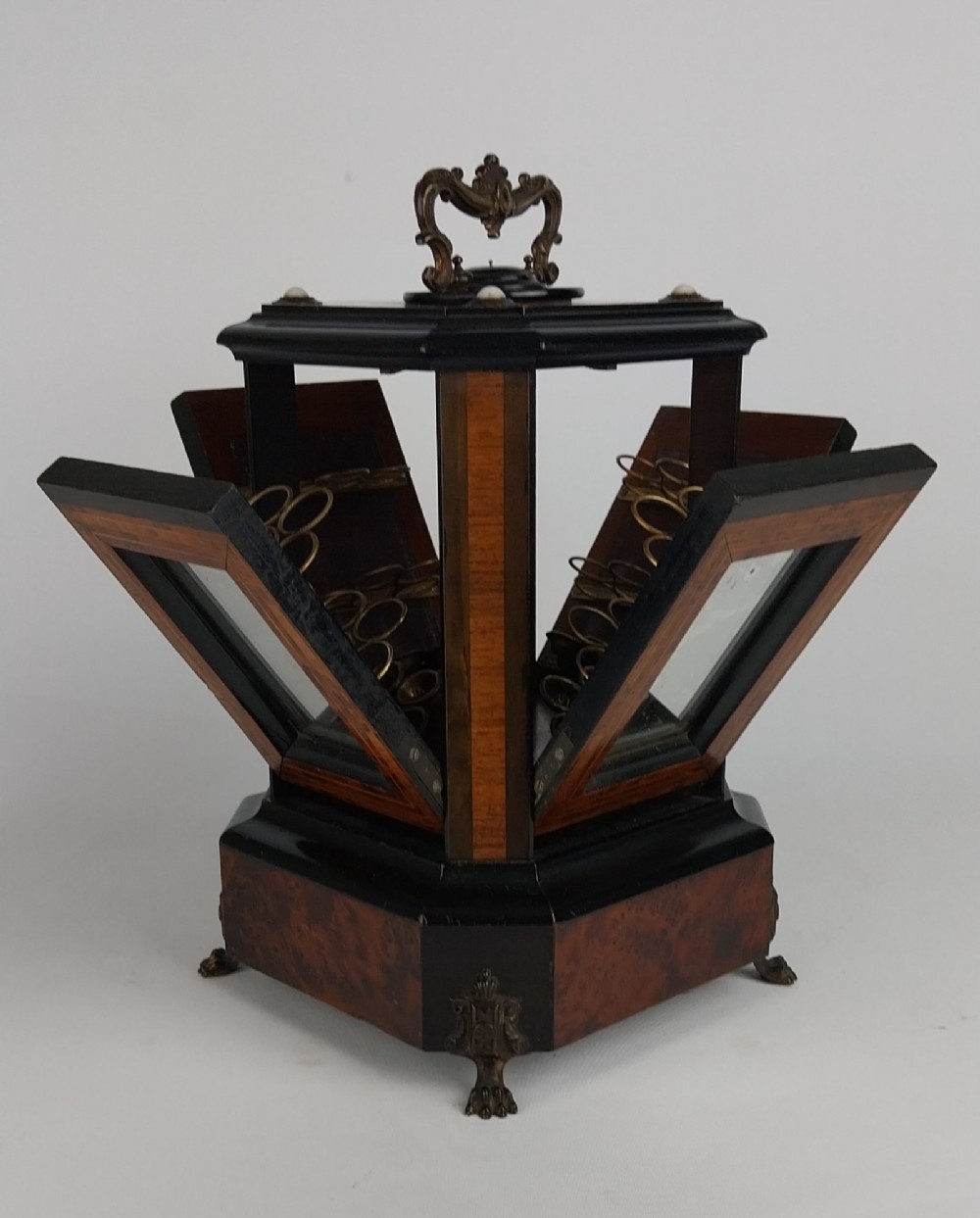An upright Victorian hexagonal musical cigar box featuring ebonised wood, burr walnut panels, glass inserts, an ornate brass top handle, and brass claw feet. View II