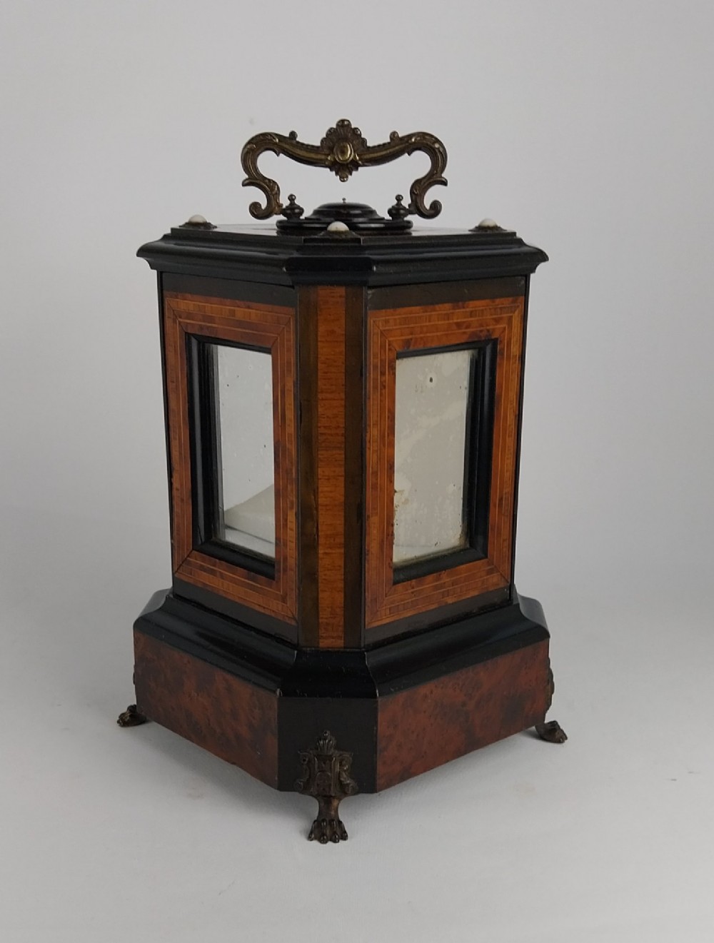 An upright Victorian hexagonal musical cigar box featuring ebonised wood, burr walnut panels, glass inserts, an ornate brass top handle, and brass claw feet. View III