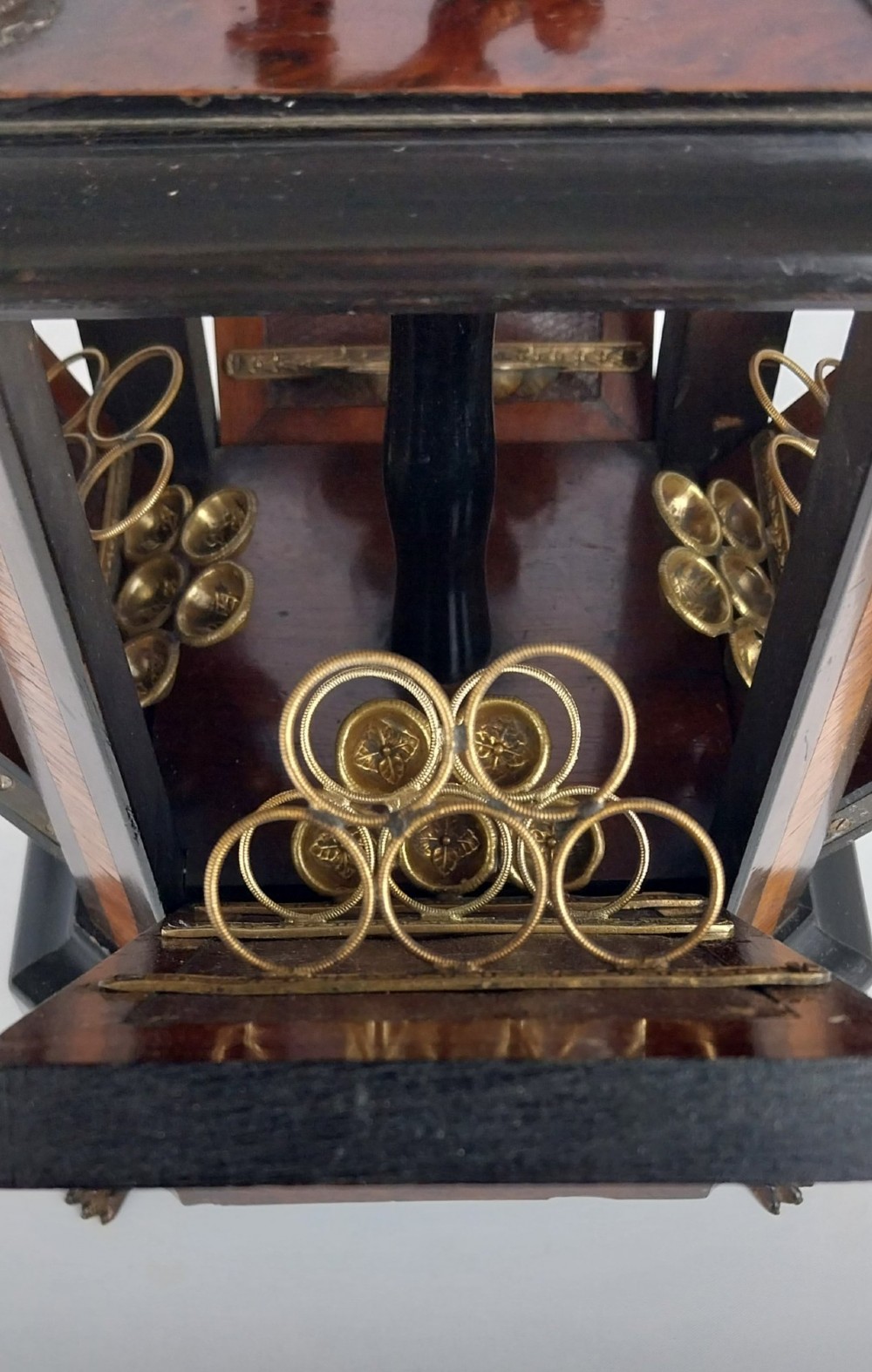 An upright Victorian hexagonal musical cigar box featuring ebonised wood, burr walnut panels, glass inserts, an ornate brass top handle, and brass claw feet. View V