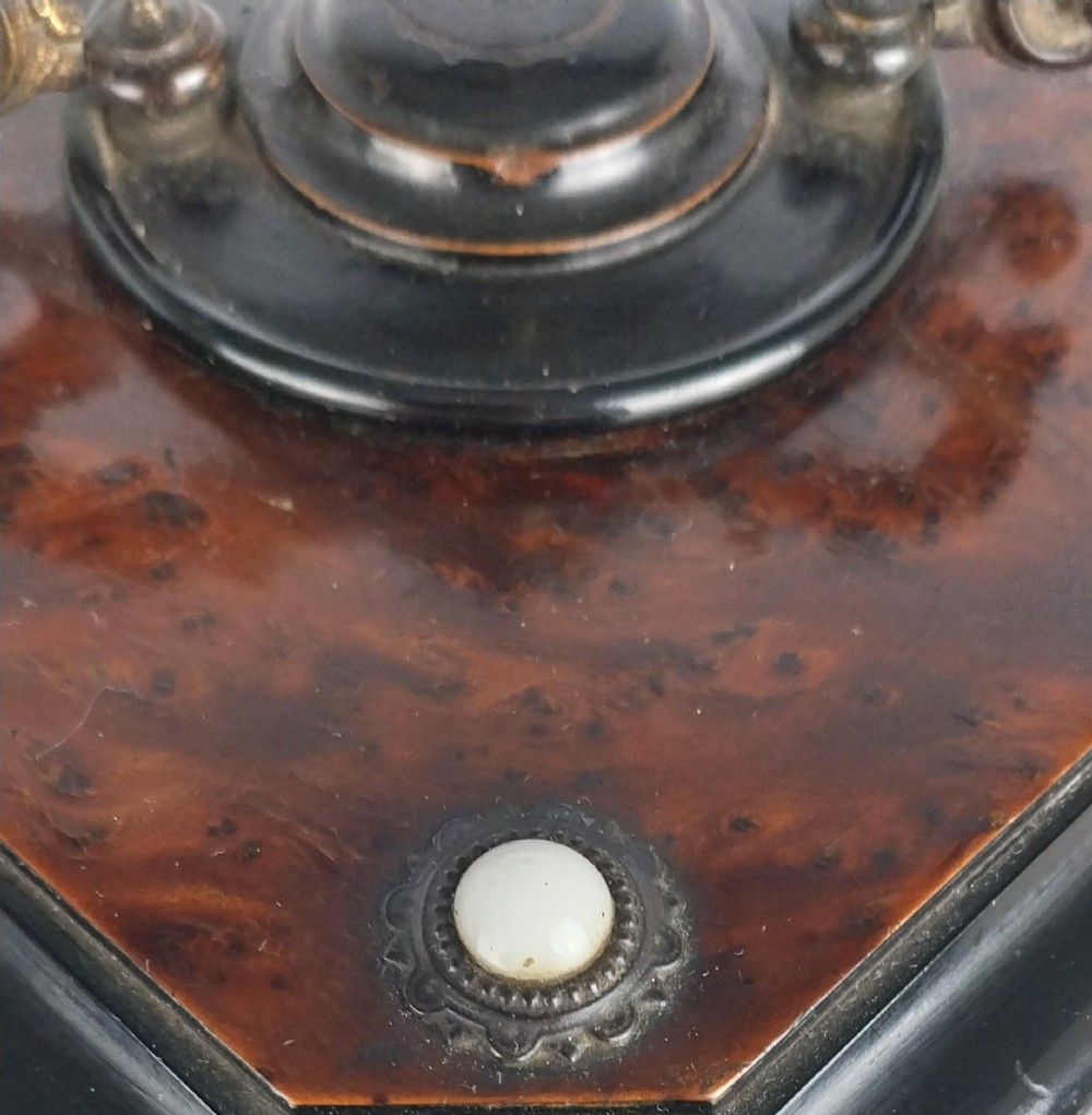 An upright Victorian hexagonal musical cigar box featuring ebonised wood, burr walnut panels, glass inserts, an ornate brass top handle, and brass claw feet. View X