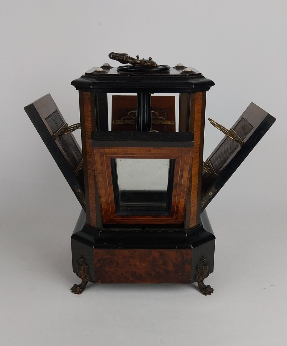 An upright Victorian hexagonal musical cigar box featuring ebonised wood, burr walnut panels, glass inserts, an ornate brass top handle, and brass claw feet. View XI