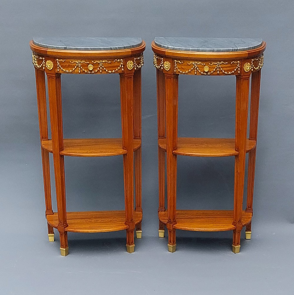 A pair of semi-circular French satinwood etagere tables featuring grey marble tops, gilt bronze garland mounts, and two lower tiers. View IV