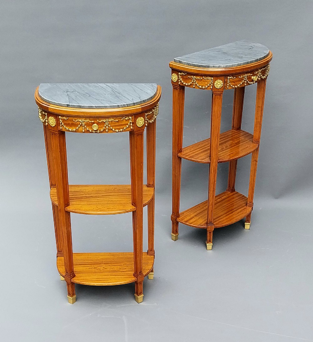 A pair of semi-circular French satinwood etagere tables featuring grey marble tops, gilt bronze garland mounts, and two lower tiers. View V