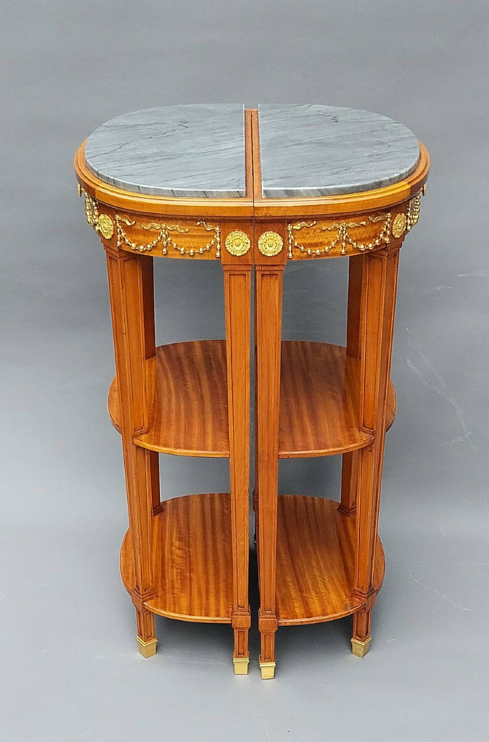 A pair of semi-circular French satinwood etagere tables featuring grey marble tops, gilt bronze garland mounts, and two lower tiers. View VI