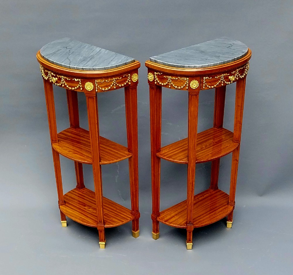 A pair of French Louis XVI style demilune side tables featuring grey marble tops, open two-tiered wooden shelving, and ornate gilt bronze floral garland mounts. View III