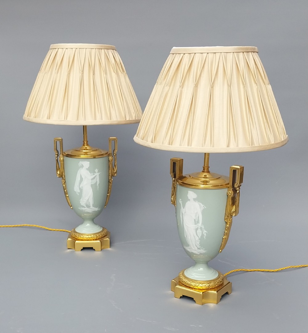A pair of 19th-century French celadon green porcelain urn table lamps featuring white pate-sur-pate classical relief figures, gilt bronze handles and bases, and cream pleated lampshades. View II