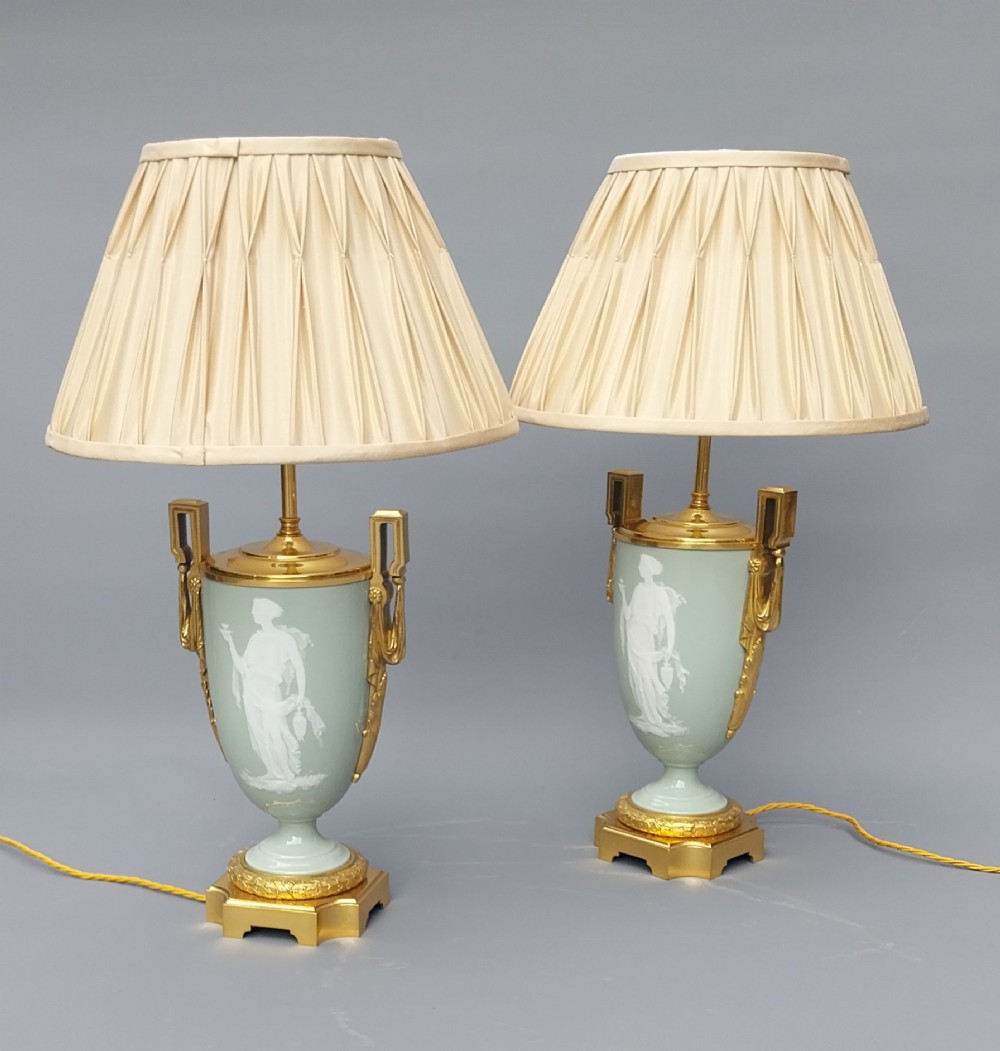 A pair of 19th-century French celadon green porcelain urn table lamps featuring white pate-sur-pate classical relief figures, gilt bronze handles and bases, and cream pleated lampshades. View III