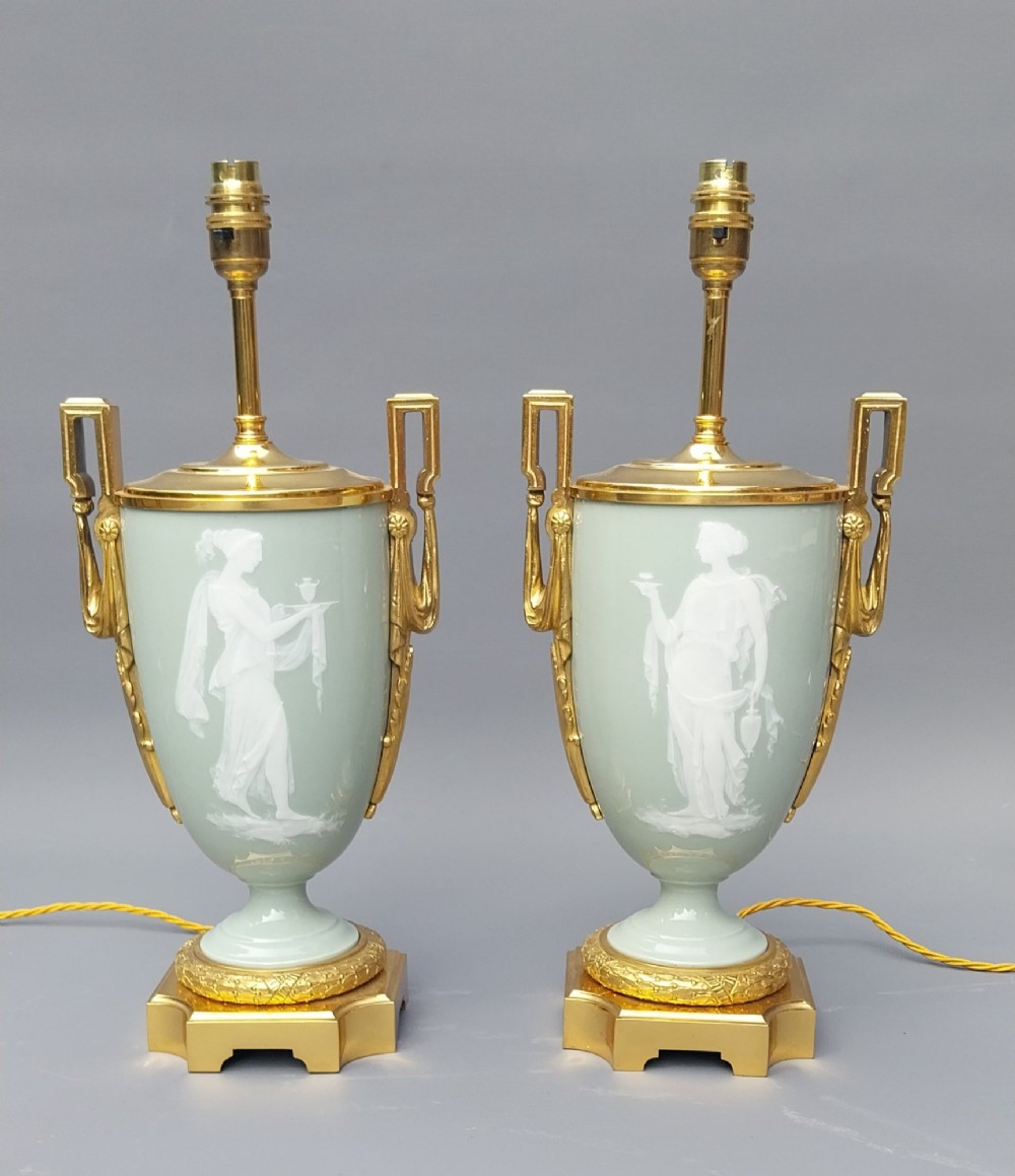 A pair of 19th-century French celadon green porcelain urn table lamps featuring white pate-sur-pate classical relief figures, gilt bronze handles and bases, and cream pleated lampshades. View IV