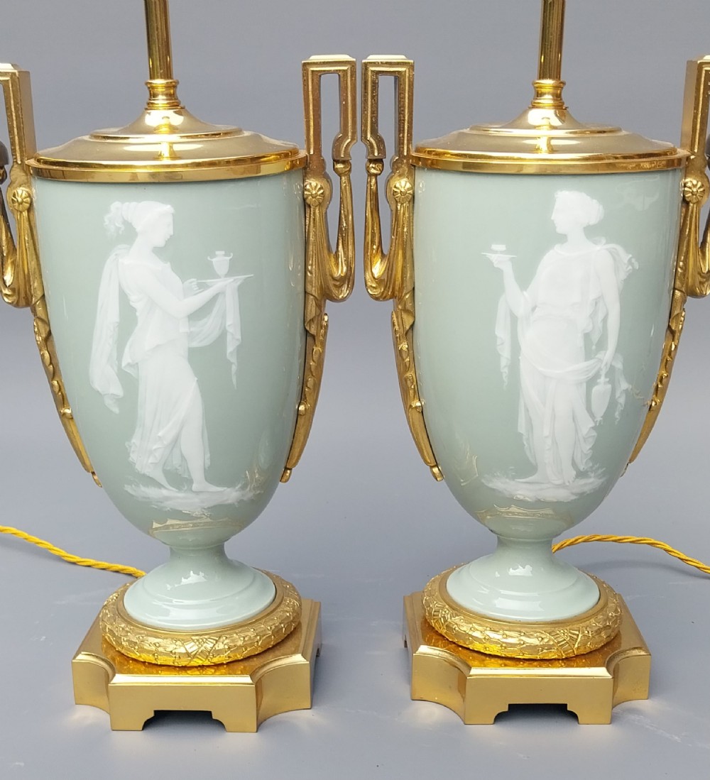 A pair of 19th-century French celadon green porcelain urn table lamps featuring white pate-sur-pate classical relief figures, gilt bronze handles and bases, and cream pleated lampshades. View VI