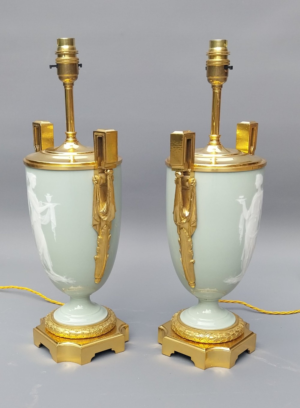 A pair of 19th-century French celadon green porcelain urn table lamps featuring white pate-sur-pate classical relief figures, gilt bronze handles and bases, and cream pleated lampshades. View VII