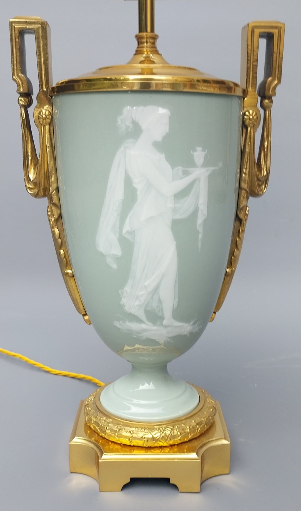 A pair of 19th-century French celadon green porcelain urn table lamps featuring white pate-sur-pate classical relief figures, gilt bronze handles and bases, and cream pleated lampshades. View X