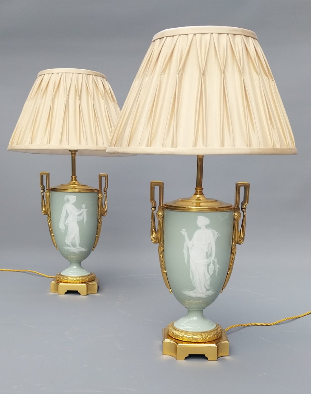 A pair of 19th-century French celadon green porcelain urn table lamps featuring white pate-sur-pate classical relief figures, gilt bronze handles and bases, and cream pleated lampshades. View XIII