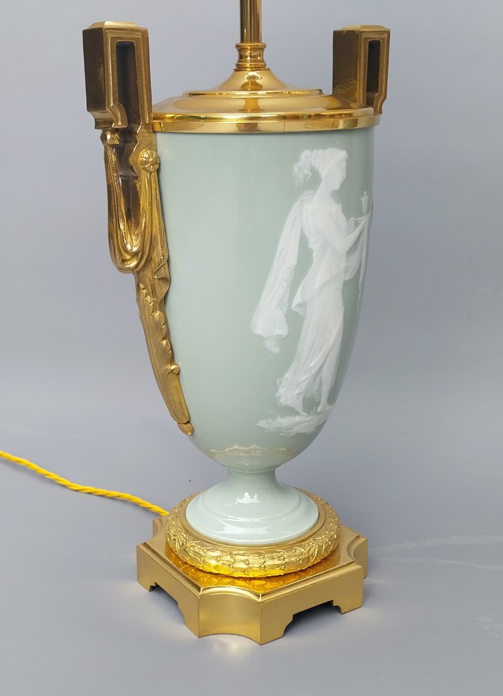 A pair of 19th-century French celadon green porcelain urn table lamps featuring white pate-sur-pate classical relief figures, gilt bronze handles and bases, and cream pleated lampshades. View XV