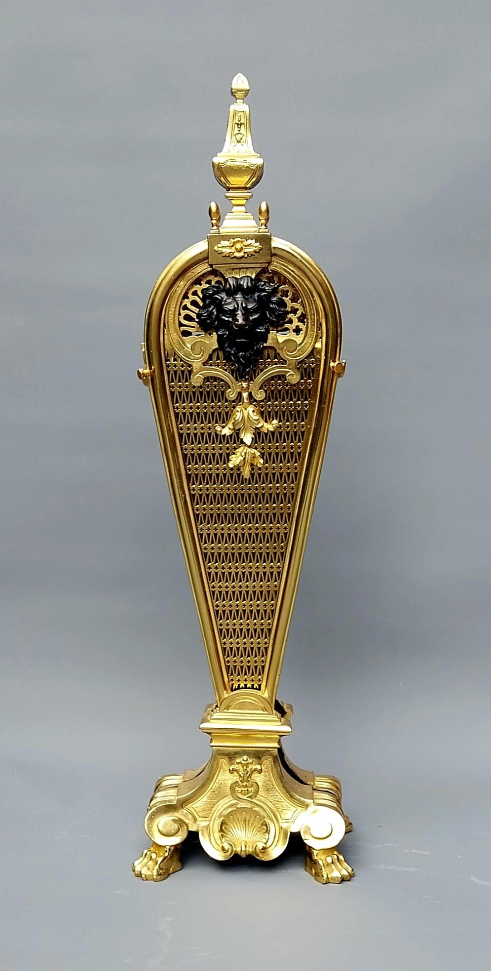 A French gilt bronze fan-shaped fire screen featuring folding filigree mesh panels, an ornate central standard with a dark mask, and a cast shell pedestal base. View II