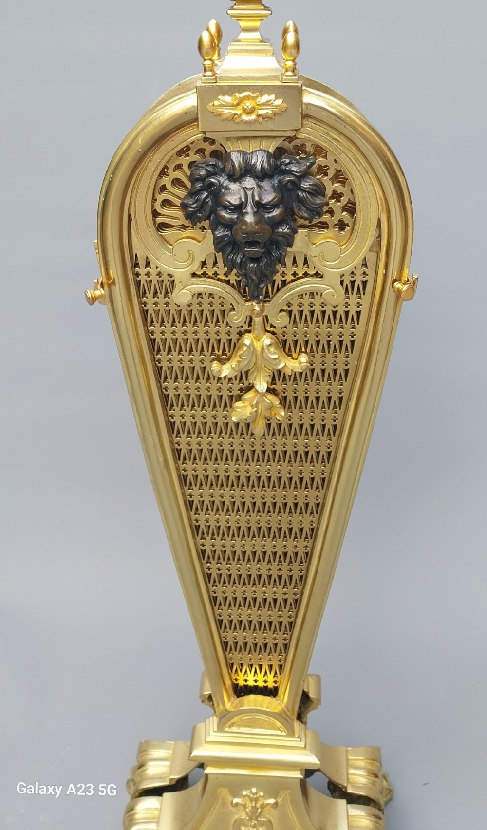 A French gilt bronze fan-shaped fire screen featuring folding filigree mesh panels, an ornate central standard with a dark mask, and a cast shell pedestal base. View V