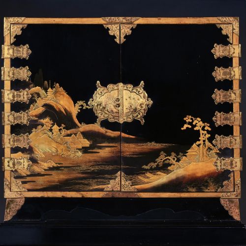 fig 1. A black lacquered Japanese cabinet decorated with gold maki-e landscape scenes, featuring ornate brass mounts and elevated on a simple black stand.