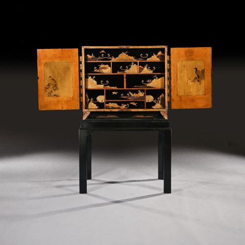 fig 2. A black lacquered Japanese cabinet decorated with gold maki-e landscape scenes, featuring ornate brass mounts and elevated on a simple black stand.