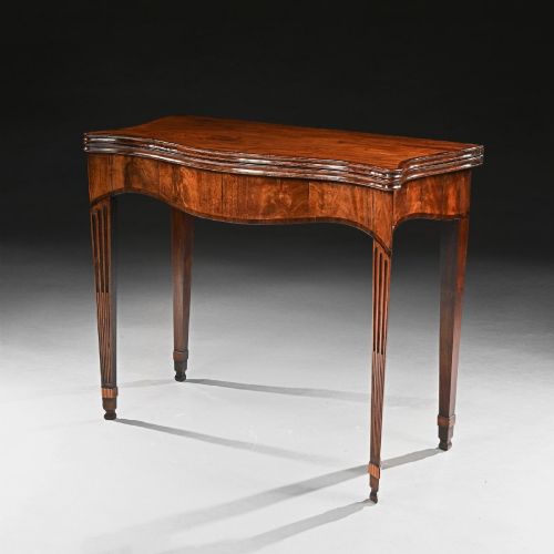 fig 2. A George III mahogany tea table featuring a serpentine fold-over top, fluted tapered legs, and flame mahogany veneers on the frieze.