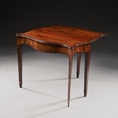 fig 3. A George III mahogany tea table featuring a serpentine fold-over top, fluted tapered legs, and flame mahogany veneers on the frieze.