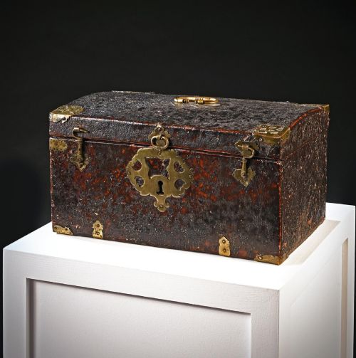 fig 2. A 17th-century dark brown leather-bound travelling box with ornate pierced brass corner mounts, side latches, central lock plate, and a top carrying handle.
